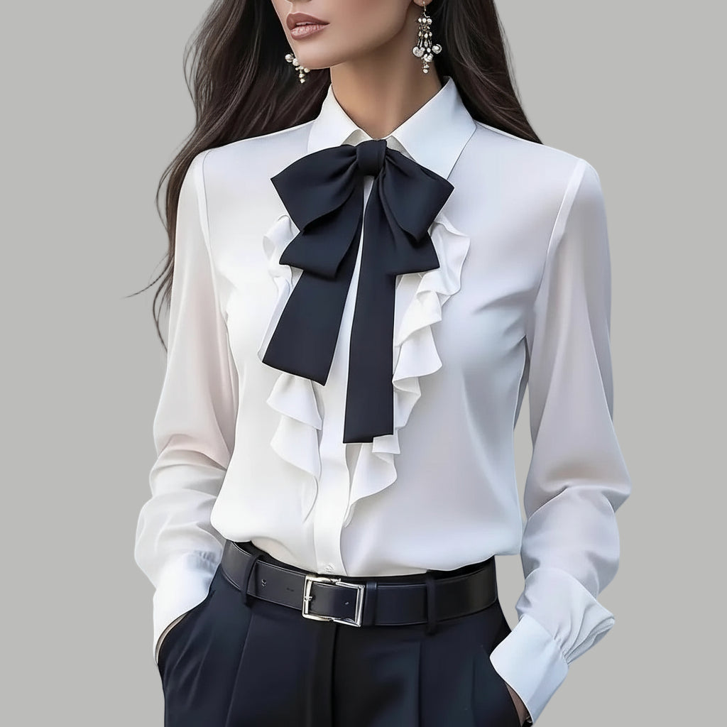 White blouse with black ruffled bow and black pants against a blurred background